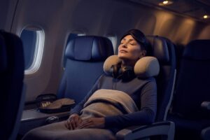 Traveler sleeping comfortably in an economy seat on a long-haul flight with a neck pillow and eye mask