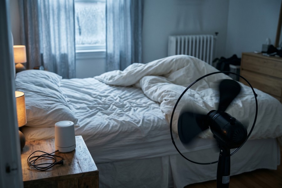 Night shift worker's bedroom with blackout curtains, white noise machine, and sleep mask on bedside table