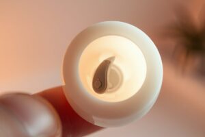 Moldable silicone ear plug putty next to a behind-the-ear hearing aid on an airplane seat