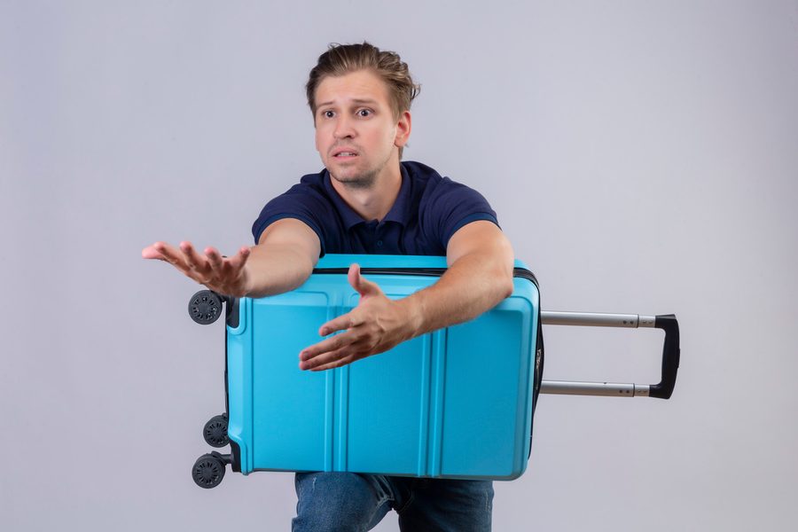 Image of a traveler at an airport check-in counter holding a suitcase with a red "overweight" tag