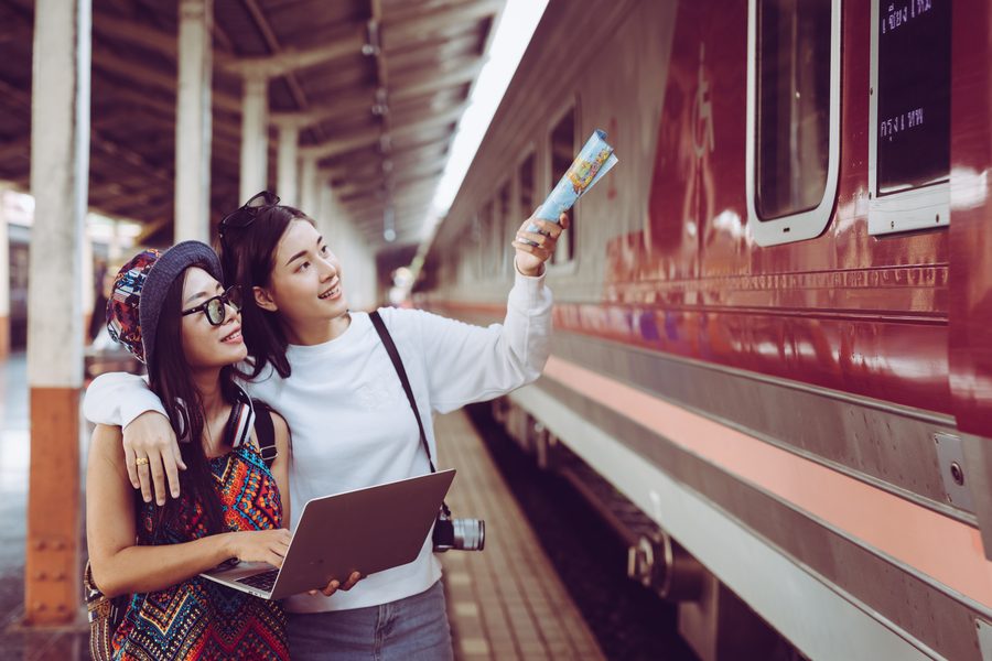 Traveler comparing train and bus ticket prices on a smartphone at Bangkok's Hua Lamphong station